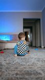Baby boy playing in the room throws his toys around. Kid sits on the floor and rolls the plastic ring by the floor. Low angle view. Vertical video.