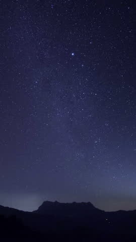 Starry night over mountain vertical time lapse video of stars in dark night sky.