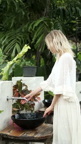 stylish woman washing her hands in a sink in a tropical garden, vertical video