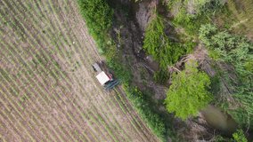 Aerial view of farmers tractor work in Tuscany agricultural fields by the creek at sunset.