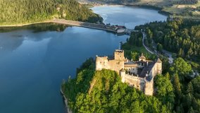 Poland. Medieval castle in Niedzica in sunset light. Artificial Czorsztyn lake on Dunajec river, damn and hydro power station. Aerial panning video from above