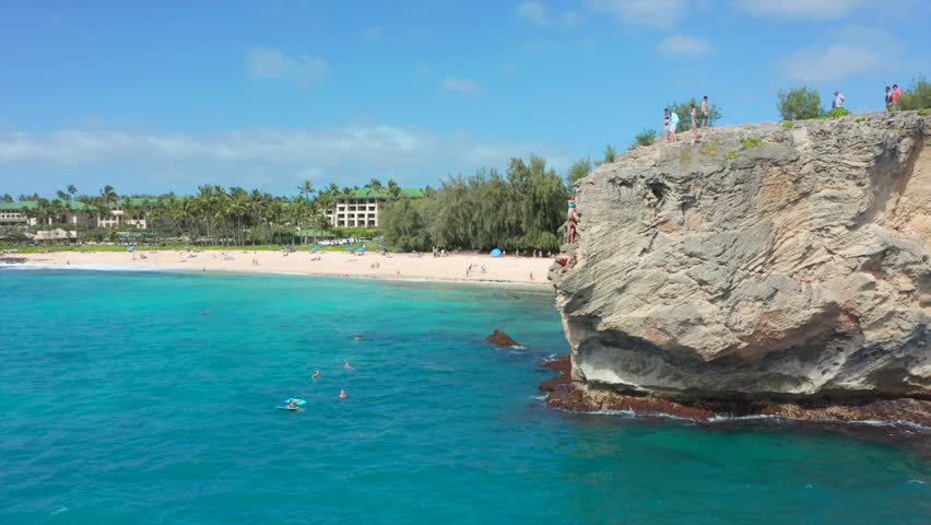 Young man doing backflip cliff jumping into ocean in Hawaii
Group of friends jumping from rocks into the ocean. Summer fun lifestyle in slow motion aerial drone shot. Poipu Kauai south shore