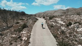 Woman cyclist riding gravel bike on gravel road in Spanish mountains. Drone flying behind a cyclist. Gravel cycling. Cyclist twists pedals on bike along mountain gravel road. Biking adventures. Spain.