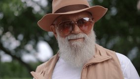 Close-up. A stylish gray-bearded elderly husband in sunglasses and a brimmed hat tastes an ice cream cone held in hand by his elderly wife, while standing outdoors in a city park in summer. A married - Powered by Shutterstock - Get 15% off with code: PIKWIZARD15