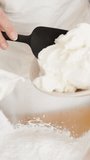 Vertical video. The pastry chef prepares cream, she adds cream cheese to the bowl with flour, in slow motion.
