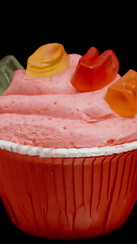 Vertical video. A cupcake with the inscription "Love" made of marmalade on pink frosting, looped rotation on a black background, isolated.