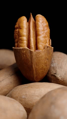 Vertical video. Half of a peeled pecan on top of a pile of nuts, close-up, rotating on a black background. Looping.