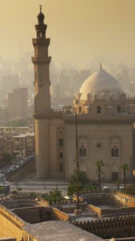 Panning shot of Mosque of Sultan Hassan, Cairo, Egypt at sunset. Cairo city in light fog in the rays of setting sun. High quality vertical shot