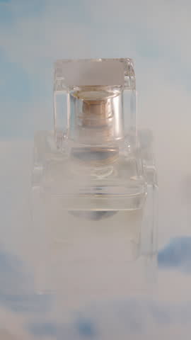 Vertical no people closeup still life of scent bottle placed on abstract background picturing bright blue sky, puffing smoke for better advertisement picture