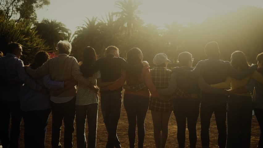 Back view of happy multigenerational people having fun in a public park during sunset time