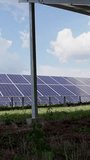 Many rows of solar panels in the green field of a solar power plant. Metal construction pillars supporting panels. Vertical video.