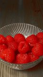 Vertical video - A large dollop of thick cream or plain yoghurt being dropped into a glass dessert bowl with fresh raspberries.