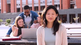 On foreground an asian schoolgirl staring front behind her multiracial friends. Young chinese teenage female student, smiling and looking at camera sitting with her classmates at university campus - Powered by Shutterstock - Get 15% off with code: PIKWIZARD15