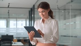 Busy middle aged mature professional business woman banking manager, 45 years old female executive or entrepreneur holding tab digital tablet standing in office at work, looking at pad. - Powered by Shutterstock - Get 15% off with code: PIKWIZARD15