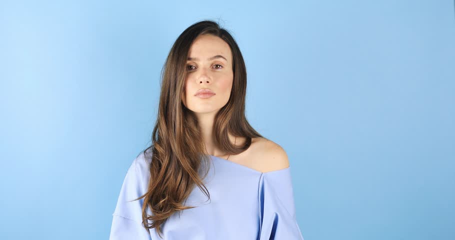 Gorgeous sensual slim tender Caucasian woman in blue pullover shake head, care cosmetics products brunette hair. Girl waving fluttering hair shaking head and fix hair isolated on blue background.