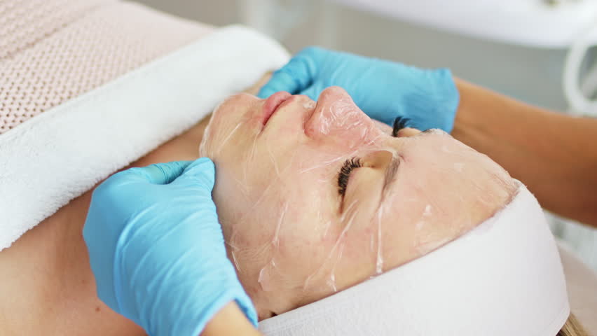 Beautician removes moisturizing mask or peeling from facial skin,   professional procedure in a beauty clinic salon for client. Skincare and cosmetology spa concept.