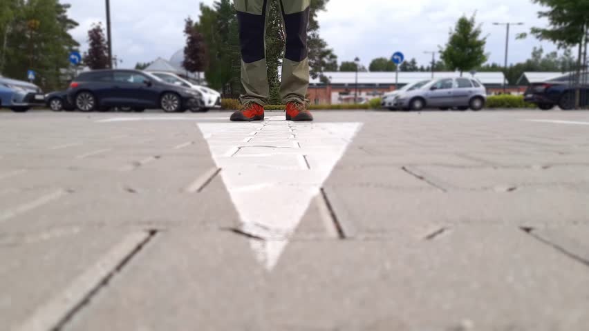 Man stands on road with white arrow show direction. Way choice concept. Feet in moccasins on road markings close-up. Indecision, waiting, choice. Person is thinking in parking near shopping center.