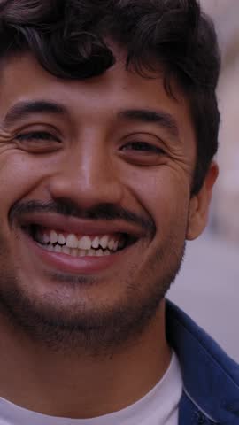 Vertical Close up face of happy young Latin man happy smiling on street. Male people with cheerful expression looking at camera in open air. Nice boy posing for photo outdoor. 