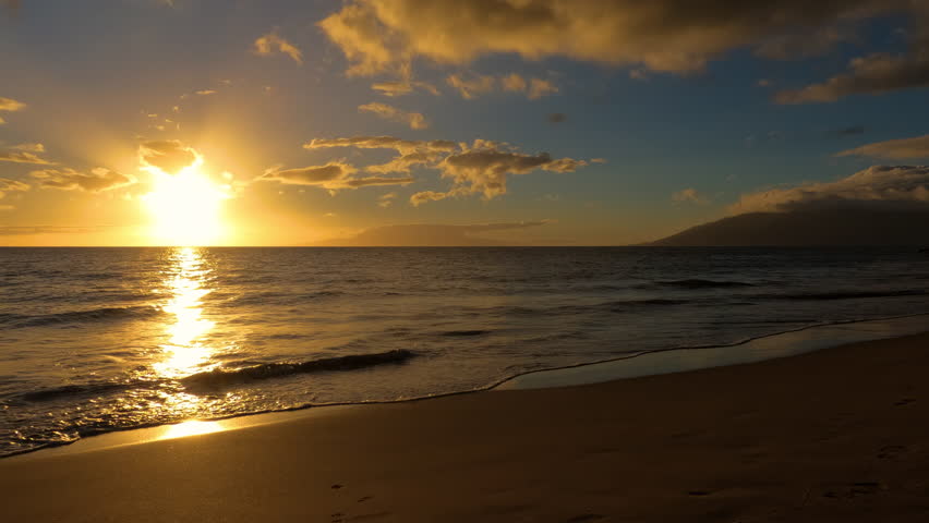 Sunset on a beach in Maui island, Hawaii. Sun going down with ocean waves slowly rolling over the sand.