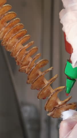 Spiral potato chips on a stick Drizzle with ketchup street food restaurant. Close-up. Potato chips spiral on a stick. Fried sweet potatoes chips, spirals on skewers on Portobello road food marke