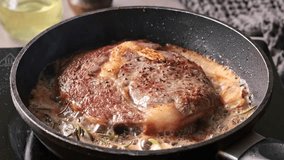 Chef pours melted butter on a juicy beef steak frying on a pan in the kitchen, close-up. Process of cooking delicious beef steak.