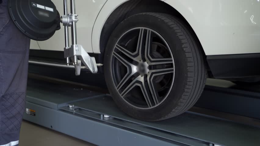 Auto technician aligns car wheel with precision equipment in garage. Vehicle maintenance, auto service, wheel alignment process shown in modern workshop. Mechanic adjusts tire sensors for balance. Royalty-Free Stock Footage #3489724071