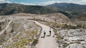 Drone view of cyclists riding gravel bikes in the scenic beauty of the mountains. Cycling on gravel roads or off-road.Active adventures and the concept of travel by bike. Gravel bike riding in nature.