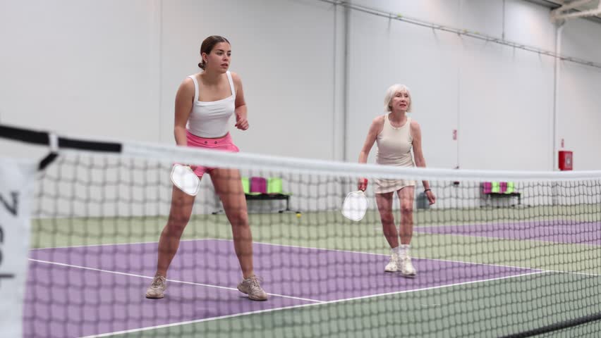 Portrait of expressive young sportswoman playing doubles pickleball with experienced female partner on indoor court, ready to hit ball. Concept of sports emotions Royalty-Free Stock Footage #3489746361