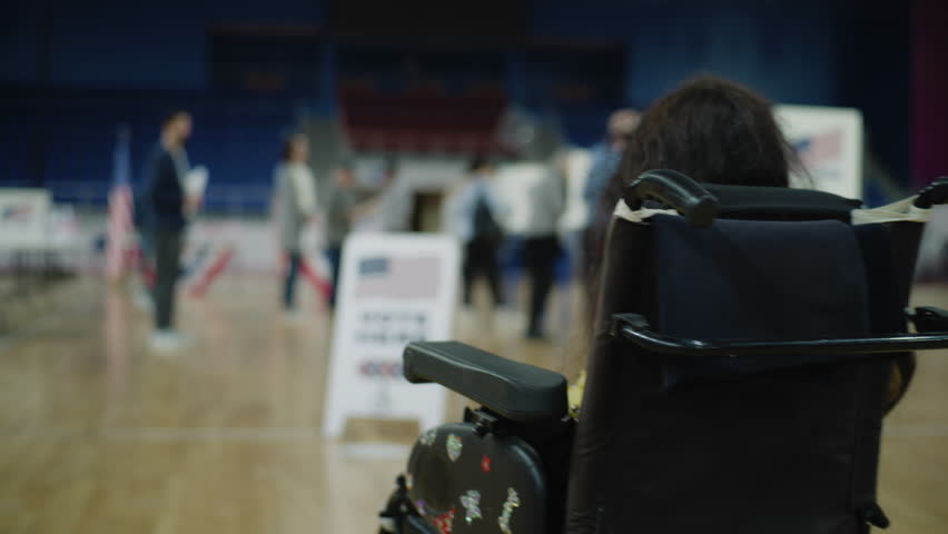 Woman with physical disability in motorized wheelchair comes to vote at polling station. Vote sign on the floor. Political races of US presidential candidates. Civic duty and patriotism. Dolly shot.
