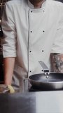 A man in a chef's uniform records the cooking process on video, standing near a frying pan in the kitchen of a restaurant