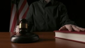 Female sitting at the desk with wooden hammer and law book, USA flag at the background. Woman judge in the court room, hitting wooden gavel, holding hand on book. - Powered by Shutterstock - Get 15% off with code: PIKWIZARD15