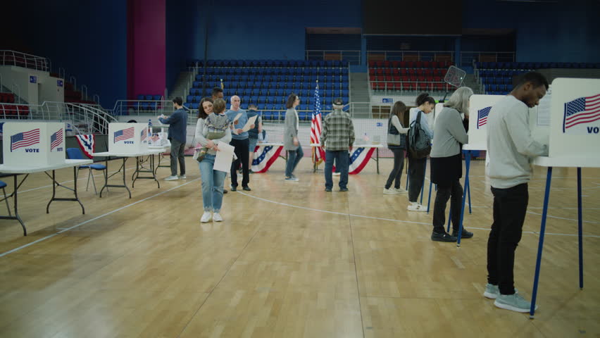 Woman with child on hands comes to voting booth. American citizens come to vote in polling station. Political races of US presidential candidates. National Election Day in United States. Dolly shot.