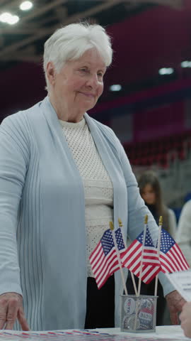 Vertical shot of Multi ethnic American citizens come to vote in polling station. Elderly woman talks with polling officer and takes vote bulletin. Political races of US presidential candidates
