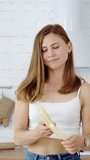 A young girl in a white kitchen peels and eats a banana. Vertical video.