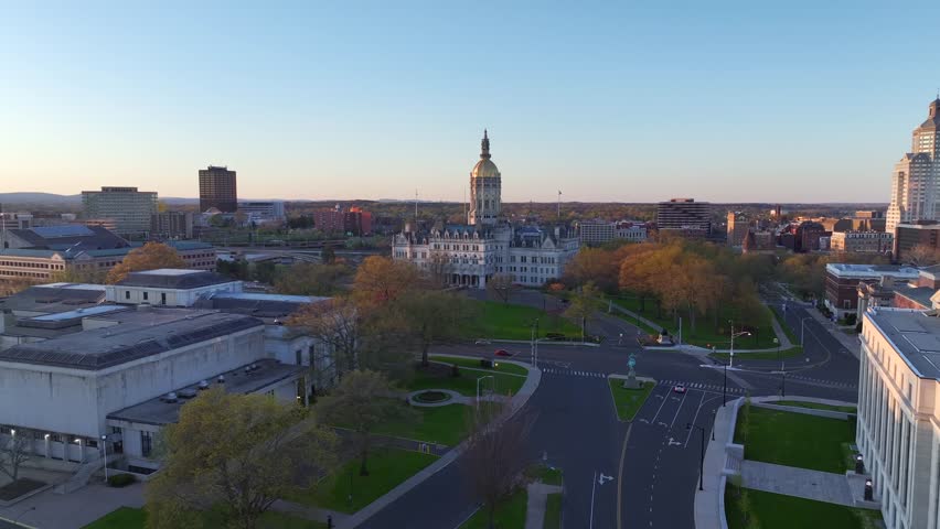 Aerial view of Connecticut State Capitol building in Hartford, CT at sunset on early spring day. Drone shot flying forward past other state government buildings towards the historic statehouse. 