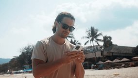On beach handsome man on vacation walks using phone. Embracing modern vacation he cherishes moments of respite and tranquility during his vacation relishing freedom and rejuvenation it brings. - Powered by Shutterstock - Get 15% off with code: PIKWIZARD15
