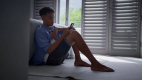 Anxious teenage boy sitting on bedroom floor at home with mobile phone concerned about bullying on social media - shot in slow motion - Powered by Shutterstock - Get 15% off with code: PIKWIZARD15