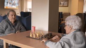 Senior women playing chess at table in canteen at nursing home
