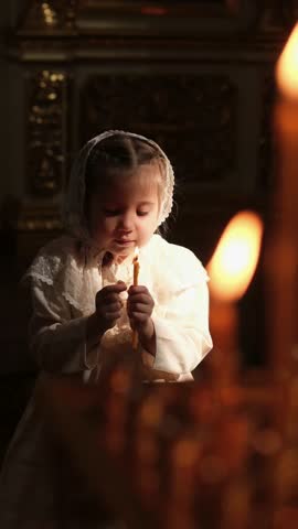 a small child, a girl in a temple or church holding a candle and praying, a child putting candles looking at the fire, introducing children to church culture Royalty-Free Stock Footage #3490584005