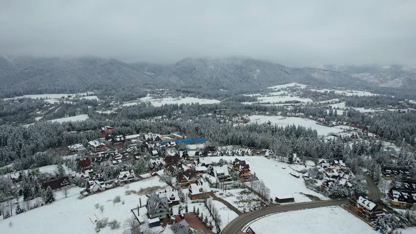 A Suburban snow-covered mountain village under beautiful mountain range. The drone circles above a snow-covered village near the mountains