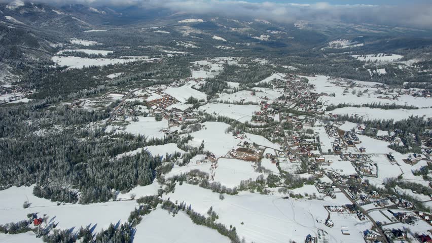 A drone captures a top view of road parking near a store. accessibility for wheelchair users and large families. The drone circles above a snow-covered village near the mountains