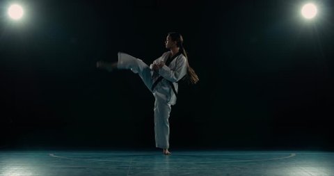 young asian girl trains martial arts taekwondo, performs kicks, slow motion, black background