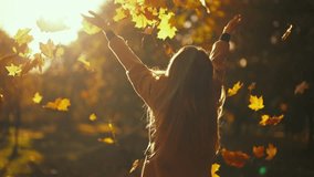 Young woman having positive good mood throwing fallen maple leaves in air in sunny autumn weather in park, back view. Outdoors leisure entertainment in fall season, playing with foliage concept. - Powered by Shutterstock - Get 15% off with code: PIKWIZARD15