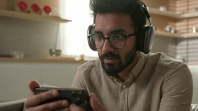 Indian Arabian man amazed excited homeowner guy in headphones watching online video sport match on smartphone at home kitchen happy male winner with mobile phone celebrate goal scream rejoice achieve - Powered by Shutterstock - Get 15% off with code: PIKWIZARD15