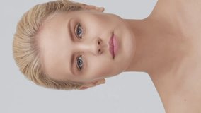 Studio portrait of young, beautiful and natural blond woman applying skin care cream. Vertical video. the concept of face lifting, cosmetics and make-up.