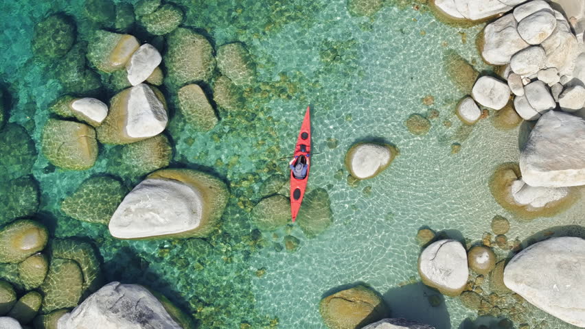 The aerial view captures a person kayaking on Lake Tahoe in California, USA. The individual paddles through the water, maneuvering the kayak along the lakes surface. 4K footage. Royalty-Free Stock Footage #3490814735