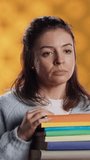 Vertical video Portrait of woman with pouting expression holding pile of books, showing disproval of reading hobby. Sulky lady with stack of novels doing thumbs down hand gesturing, studio background