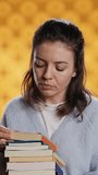 Vertical video Portrait of woman browsing through stack of textbooks, gathering information for school exam, isolated over studio background. Person searching necessary course for exam in pile of