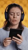 Vertical video Voice actor frowns while reading ebook, portraying character, studio background. Woman reenacting digital recording of novel, interpreting furious antagonist, reading text from tablet