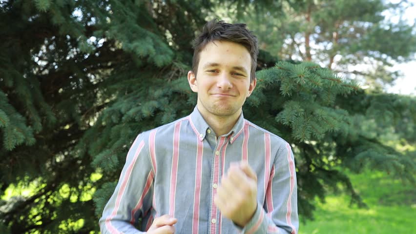 Smiling Young Man Giving Two Thumbs Up in Lush Park on a Sunny Day